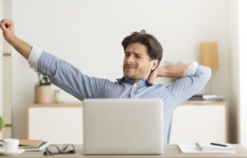 Man Stretching Hands Sitting At Laptop Excercising Tired Of Working Or Studying At Home